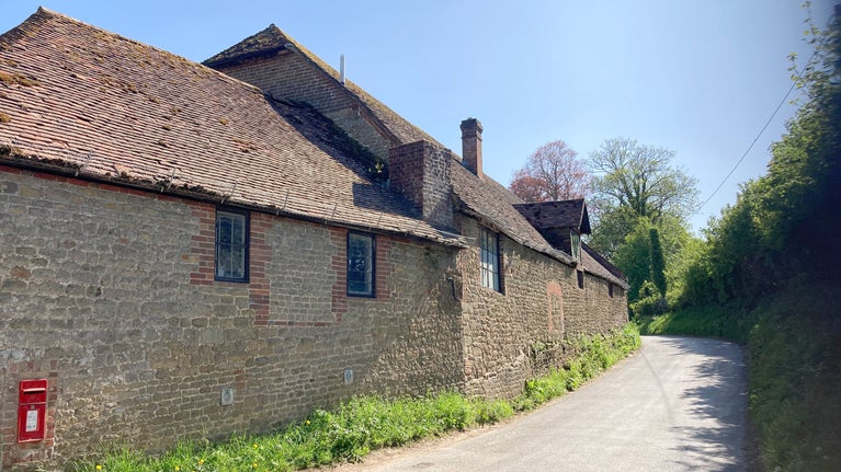 The side of a period brick building on the left side of a narrow, curving country lane.
